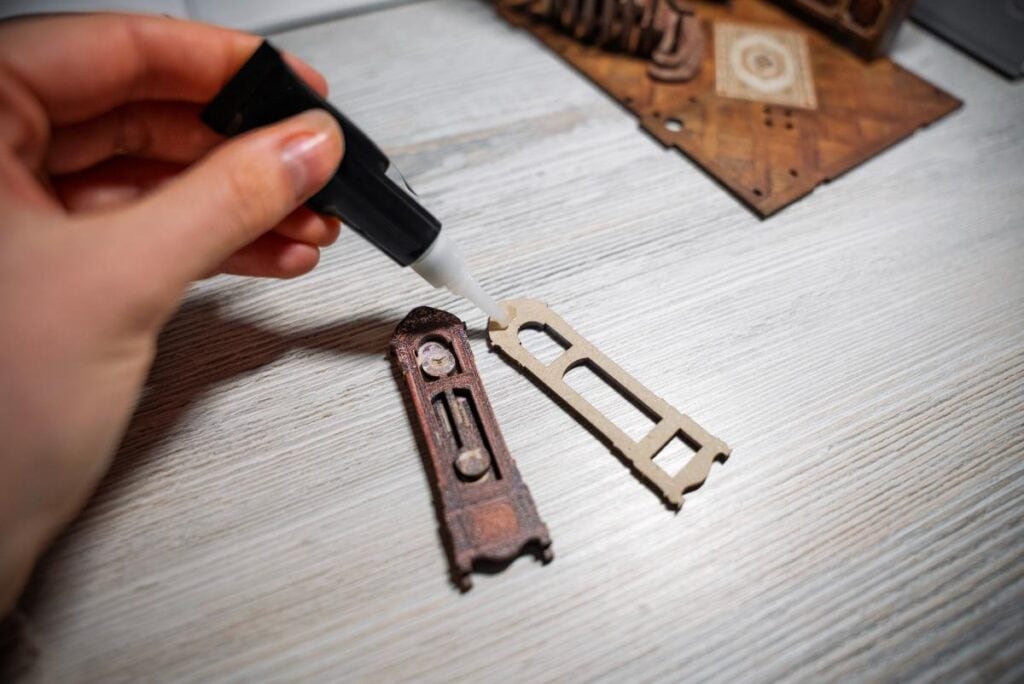 Close-up of a hand gluing small wooden pieces for a DIY miniature book nook project, showing detailed craft assembly.