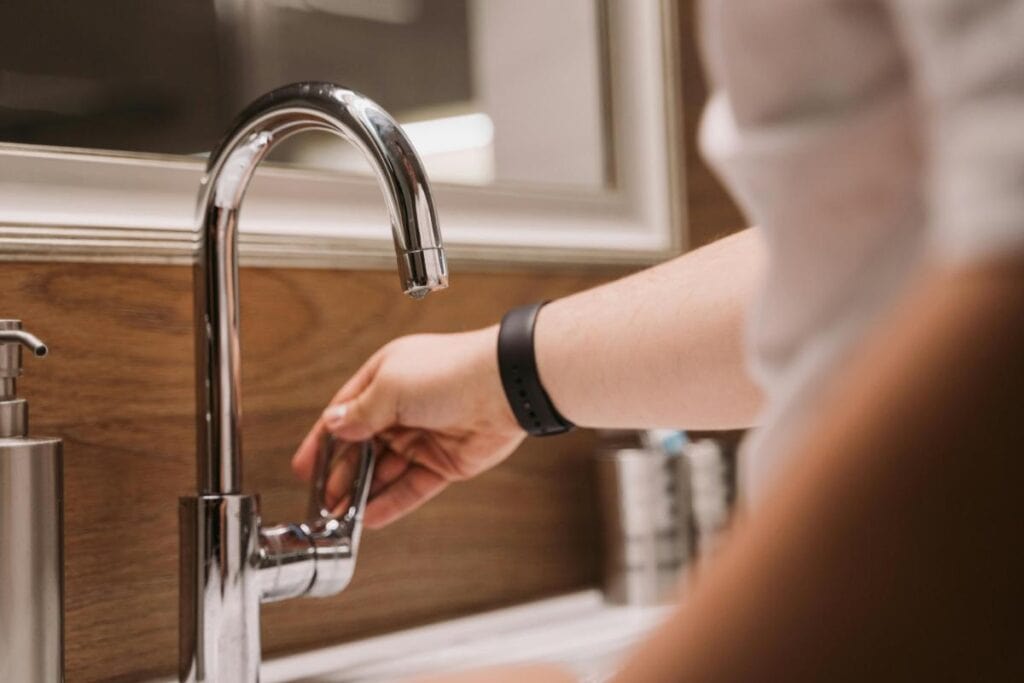 Person adjusting a modern kitchen faucet handle over a sink, illustrating everyday kitchen plumbing use and water control.