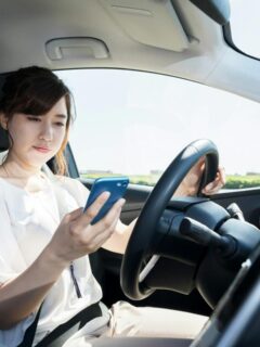 Woman looking at a mobile phone while driving a car, representing risky distracted driving behavior and reduced road safety.