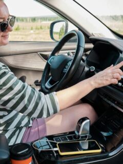 Driver using the touchscreen dashboard inside a modern car while parked outdoors during a family road trip.