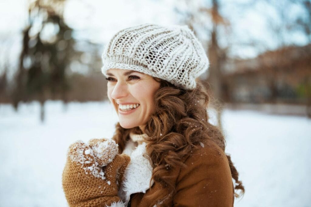 stylish woman in hat, coat, scarf, and gloves in snowy landscape