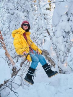 woman in a yellow coat sitting on tree in snowy landscape