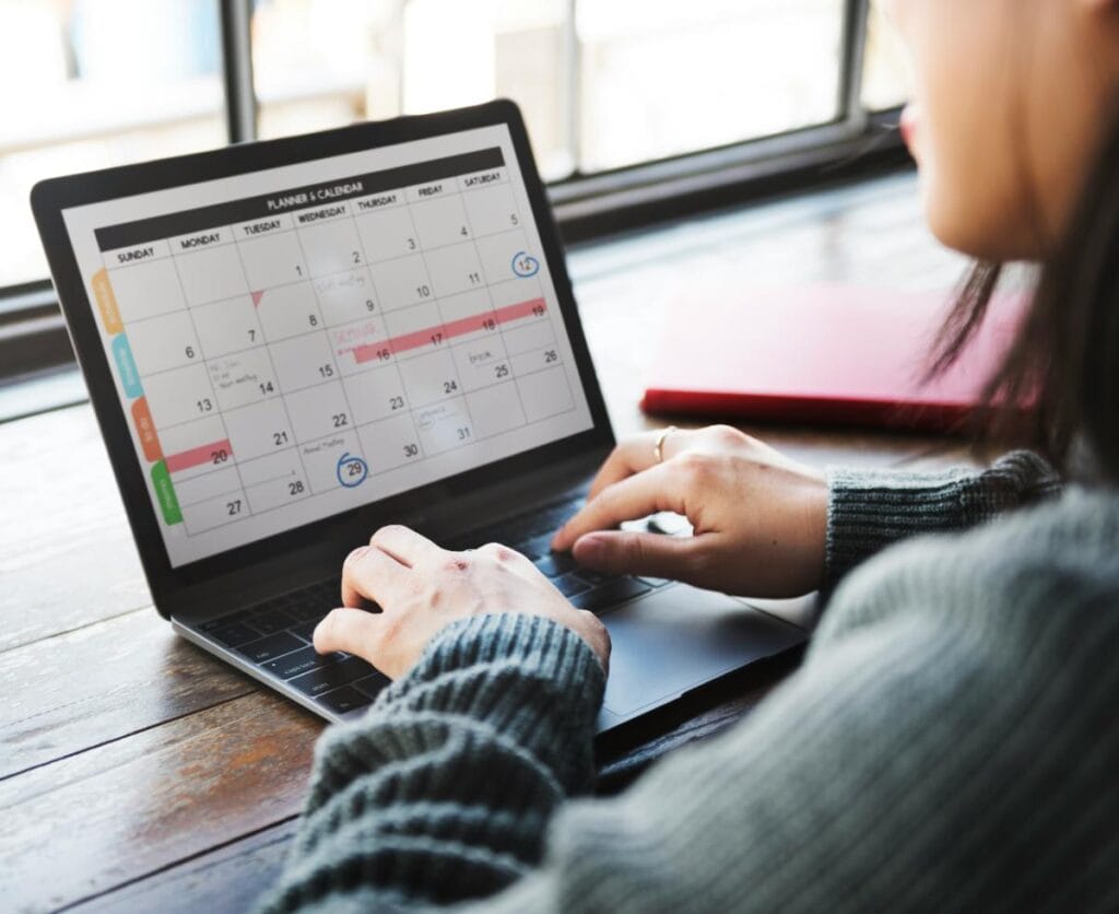 woman using laptop and calendar to plan her month