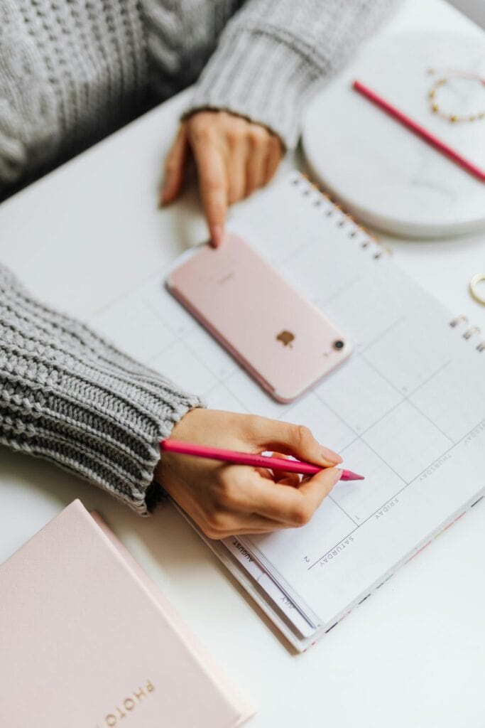 woman using phone and planner to plan monthly routines