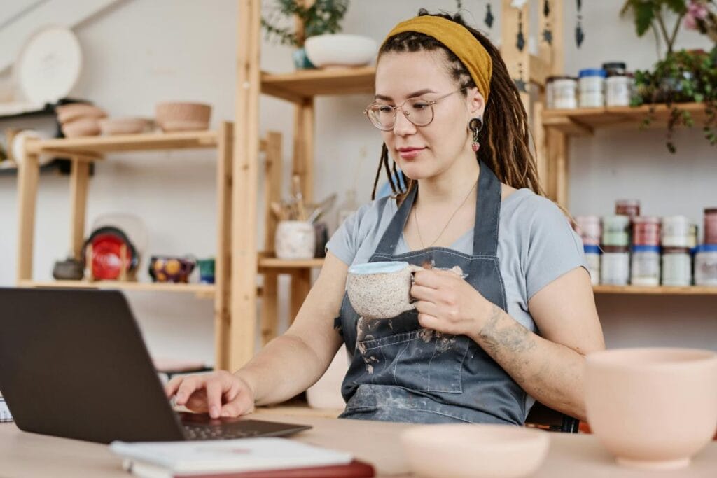 small business owner using laptop and drinking coffee in her art studio