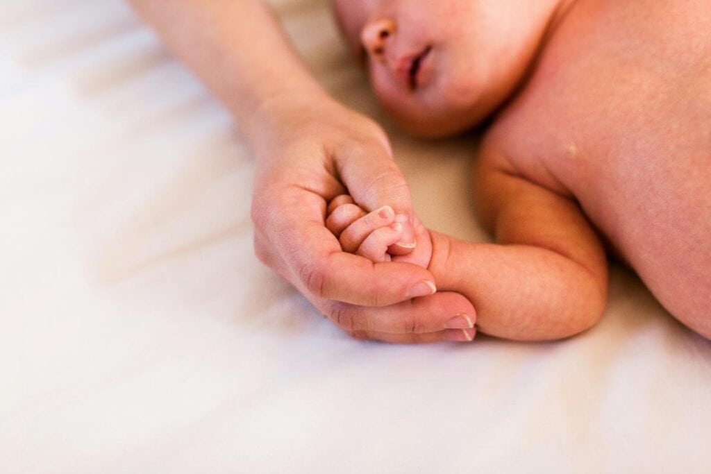 Close-up of a newborn baby holding an adult&rsquo;s finger, symbolizing parental care, bonding, and support during the first year of life.