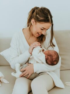 Mother smiling while cradling her newborn on a sofa, capturing a tender moment of connection and early parenthood.