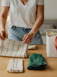 Individual folding and sorting household linens on a table, representing everyday organization practices that contribute to a calmer and healthier lifestyle.