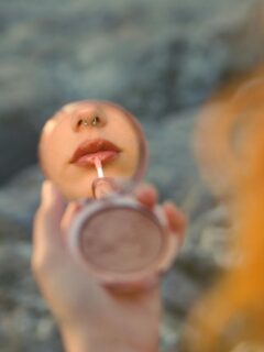 woman applying lip oil while looking into a compact