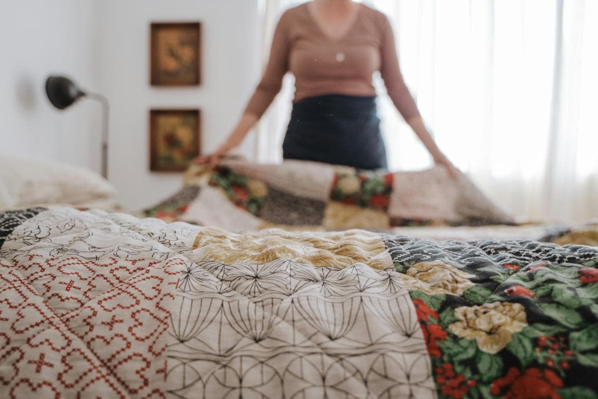 woman placing quilt on bed