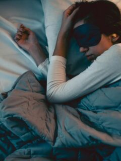 Person sleeping comfortably under a weighted blanket while wearing a sleep mask and earplugs, creating an ideal environment for restful sleep.