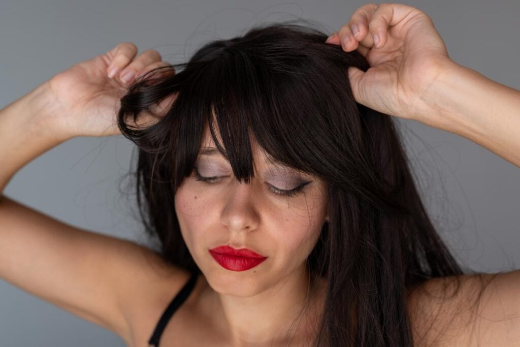 Woman adjusting the fit of a dark brown wig by positioning it around her hairline for a secure and comfortable fit.
