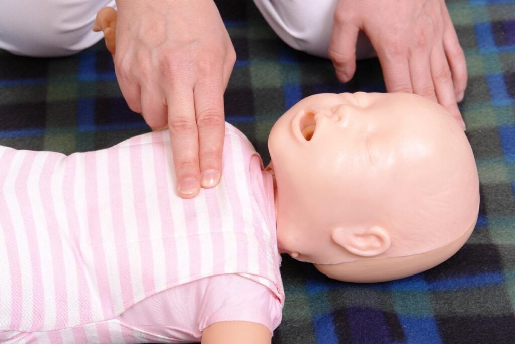 Instructor demonstrating infant CPR on a baby training mannequin during a first aid class.