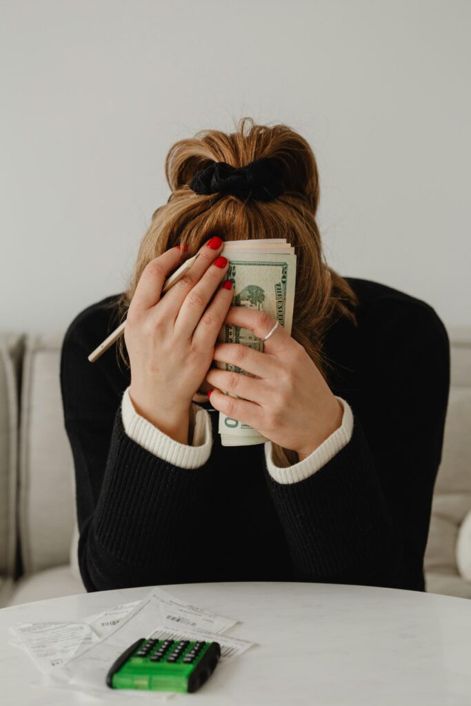 Person holding cash and covering their face while sitting at a table with bills and a calculator, representing the financial stress of borrowing money.