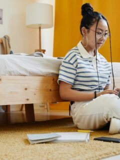 young female college student sitting in dorm room floor with laptop