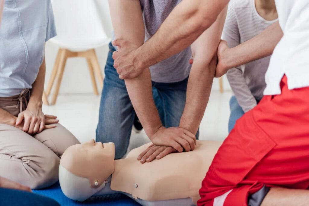 Students practicing adult CPR chest compressions on a training mannequin with an instructor.