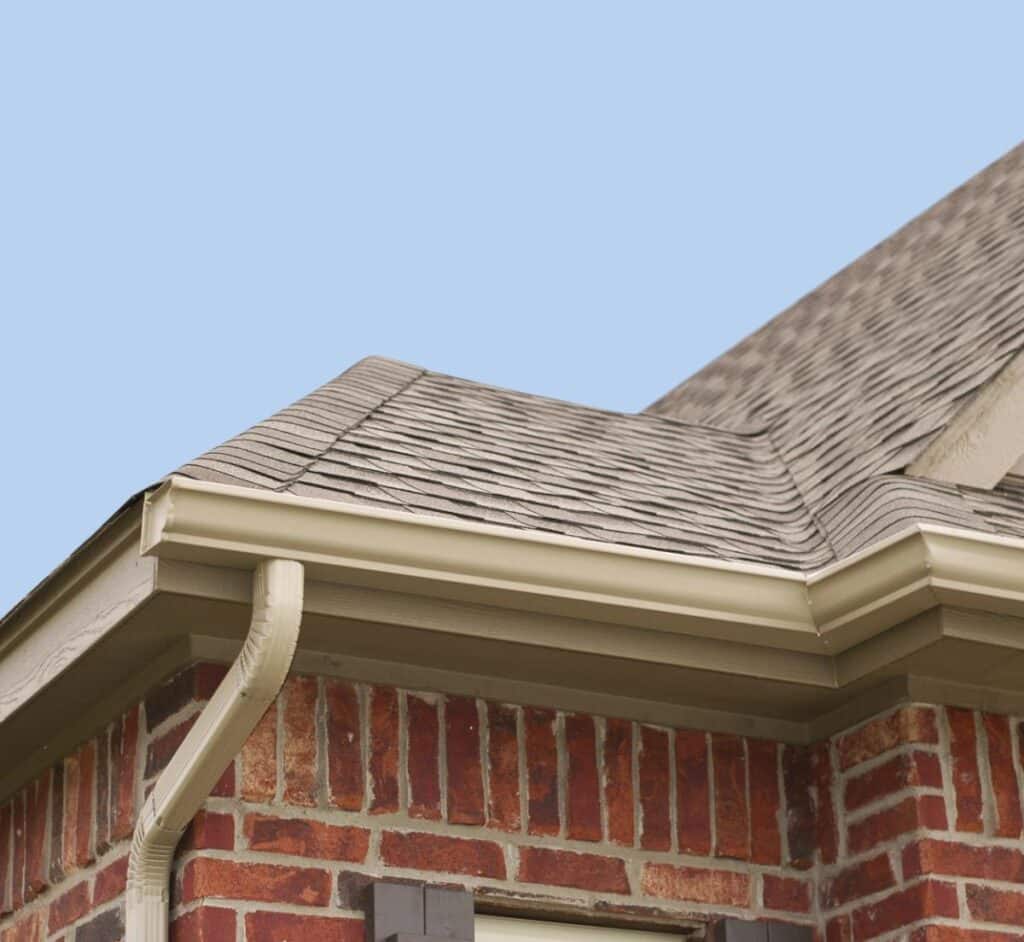 a brick house's roofline, gutter, and downspout against a light blue sky