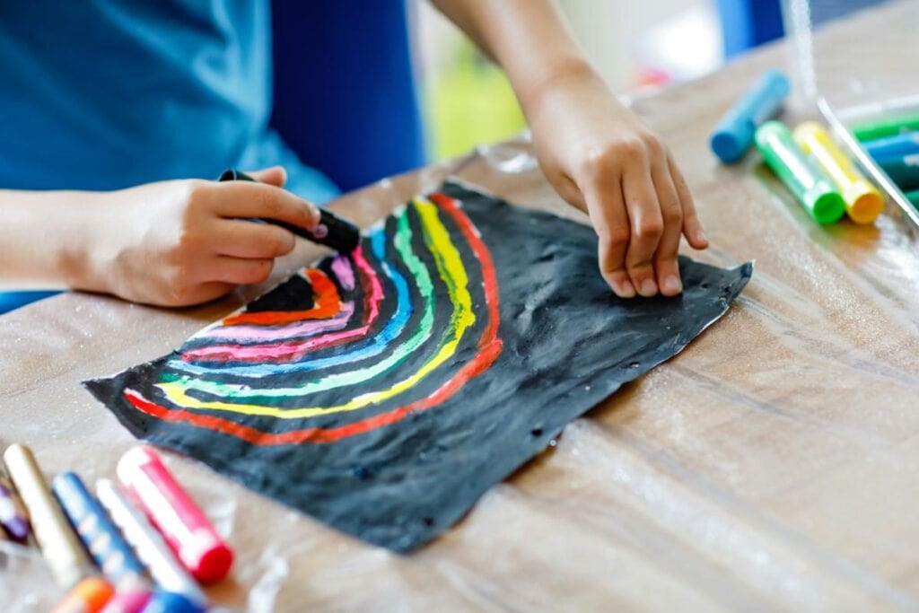 Child drawing colorful rainbow artwork with markers on black paper