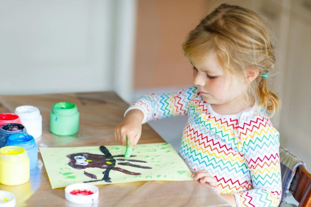 Young child painting a colorful artwork at home with finger paints