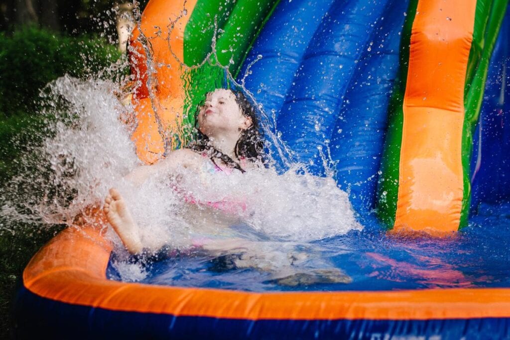 Child splashing into the pool at the bottom of a colorful inflatable water slide, demonstrating safe, active outdoor play and summer entertainment.