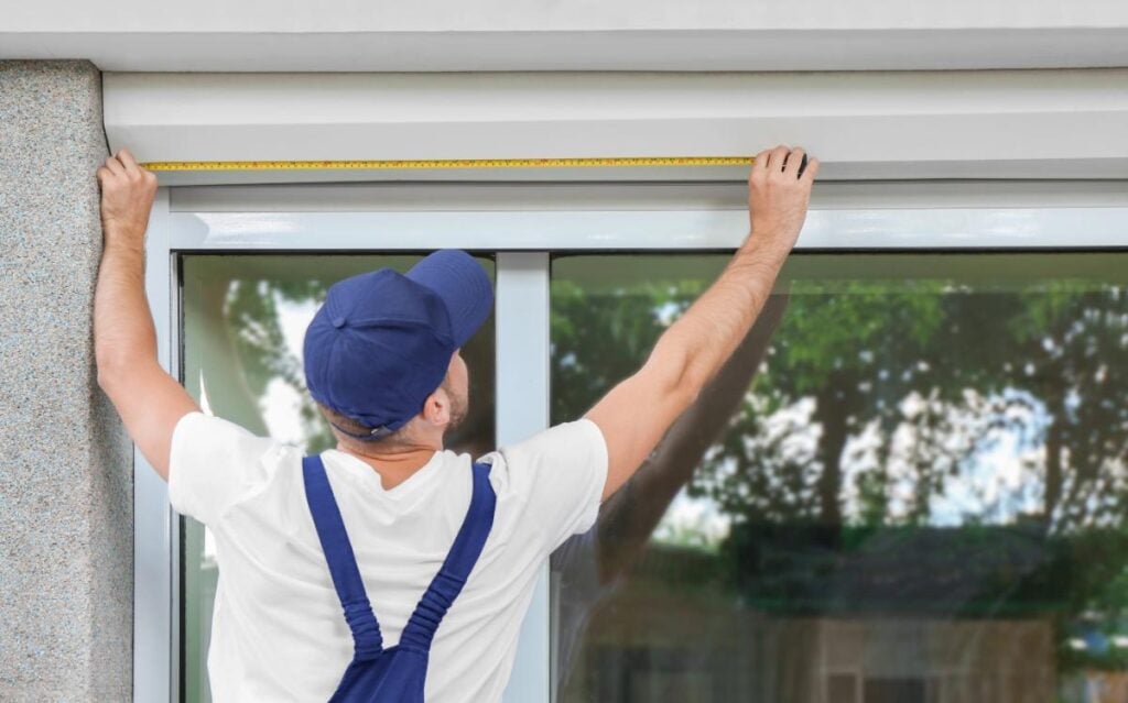 Installer measuring a window for outdoor blind installation.