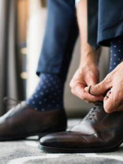 Man tying brown leather dress shoes while wearing a smartwatch and dress socks.