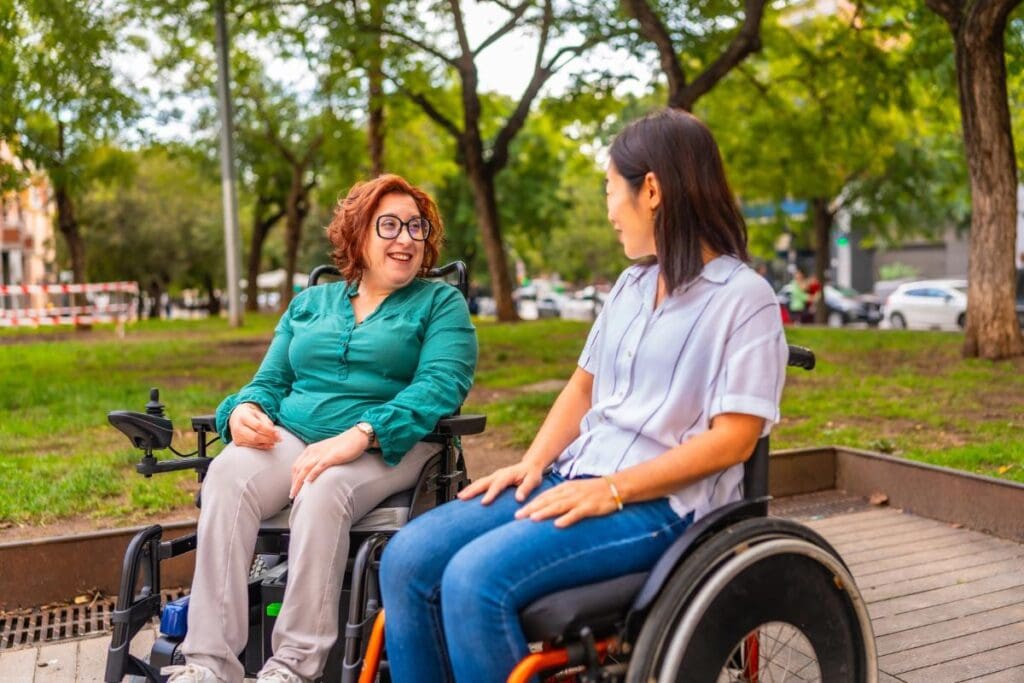 Two wheelchair users chatting together in a park, highlighting mobility and independence.