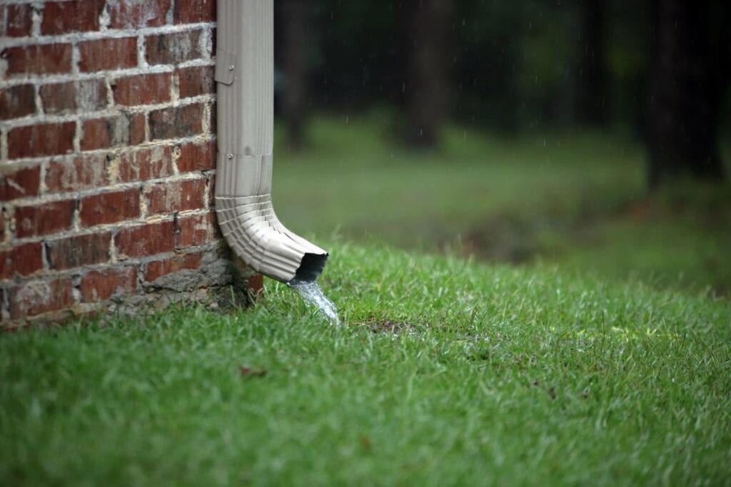 rainwater coming out of a downspout against brick house