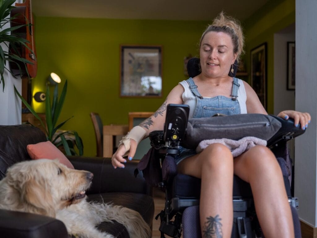 Person using a power wheelchair at home while interacting with their dog.