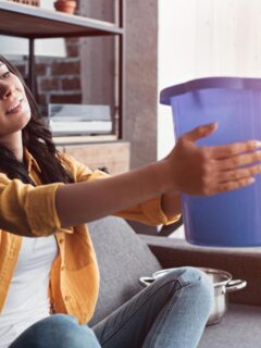 Homeowner placing a bucket under a ceiling leak to catch dripping water indoors.