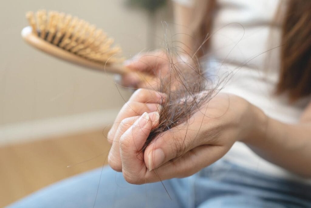 Person holding loose strands of hair after brushing, illustrating hair loss during treatment.