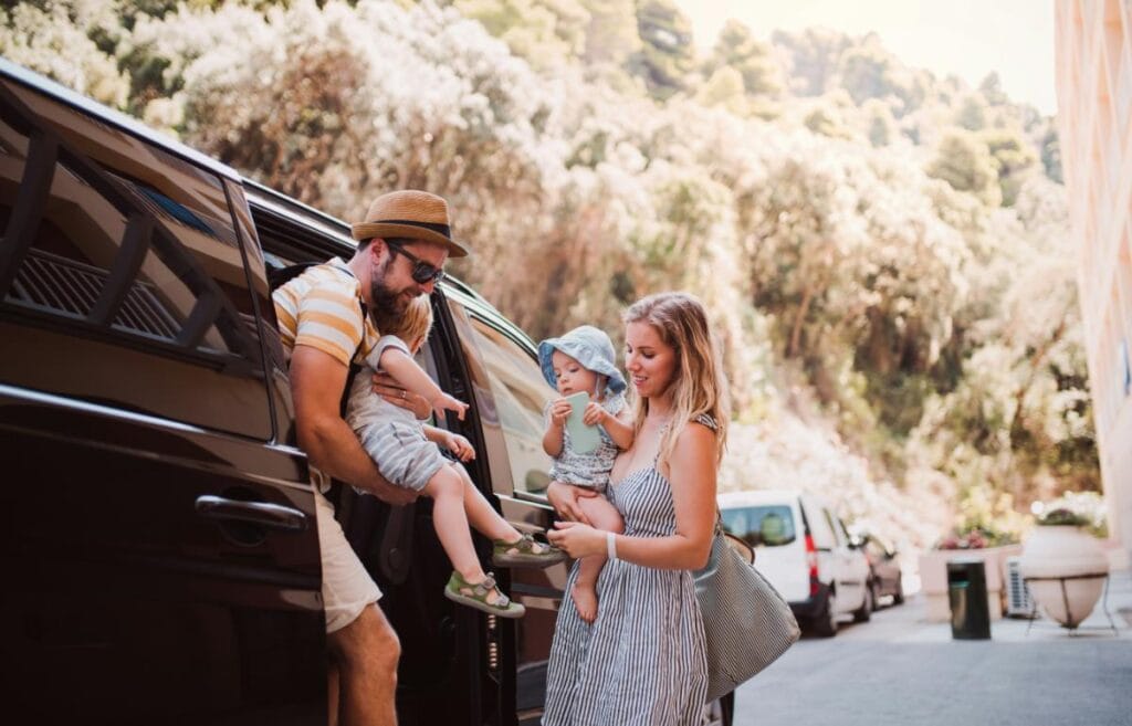 Parents unloading two young children from a van during a family trip.