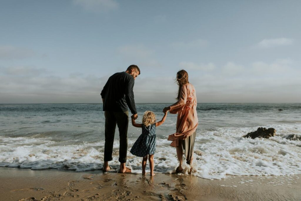 family of three holding hands at the beach by the water's edge