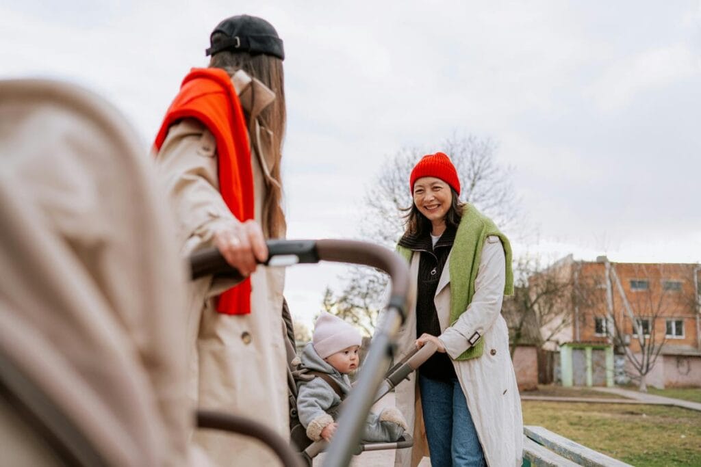 Two women chatting outdoors while a baby sits comfortably in a stroller.