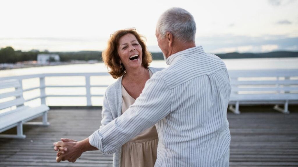 Smiling retired couple dancing by the waterfront.