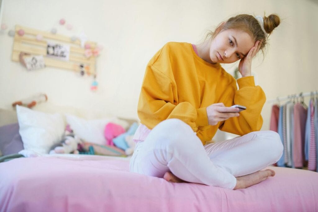 Child looking thoughtfully at a smartphone in their bedroom.