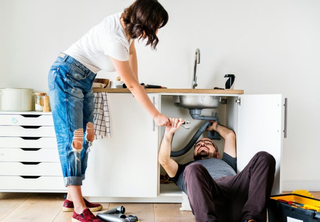 Homeowner repairing a leaking kitchen sink with plumbing tools