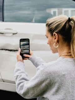 woman taking pics of car damaged after auto accident