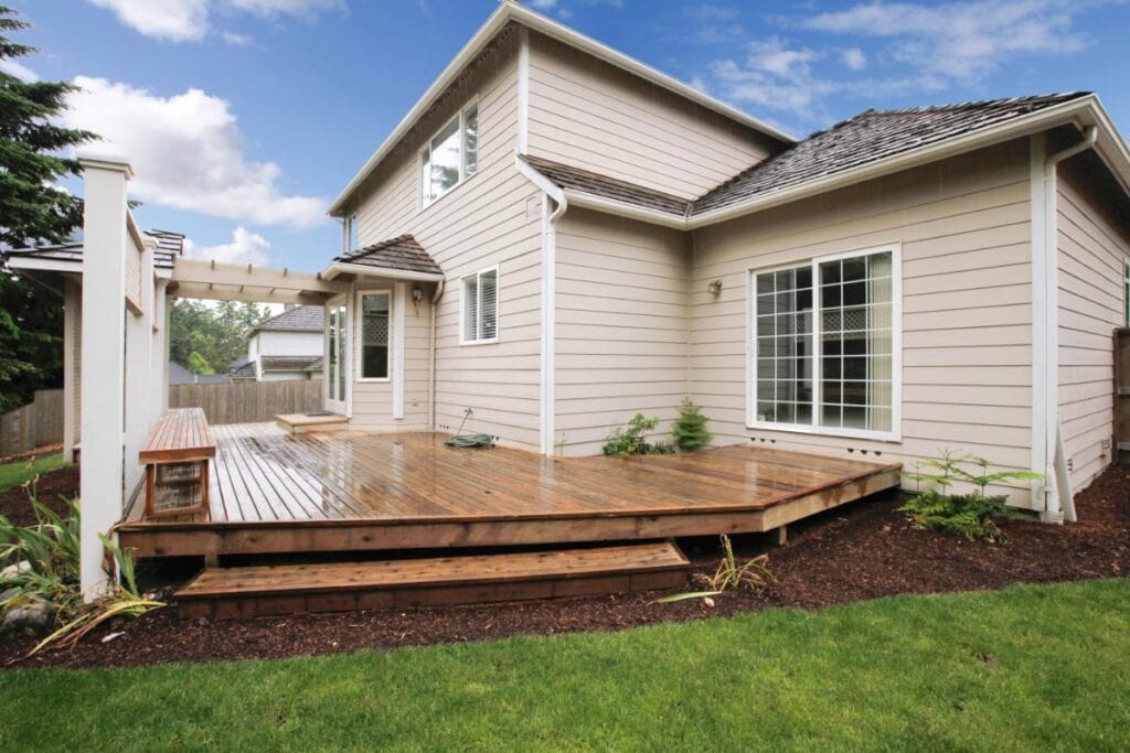Spacious wooden backyard deck beside a two-story home.