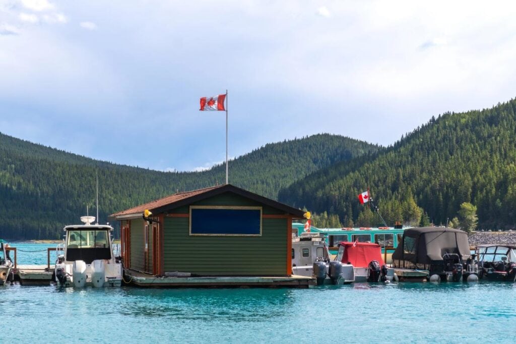 Boats docked beside a floating boathouse with Canadian flags and forested mountains
