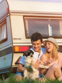 happy couple and dog sitting outside their caravan
