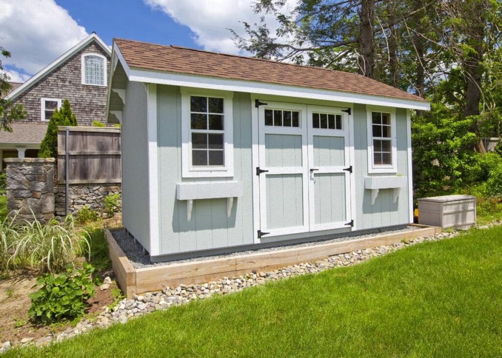 Light gray garden shed with double doors and windows beside a green lawn