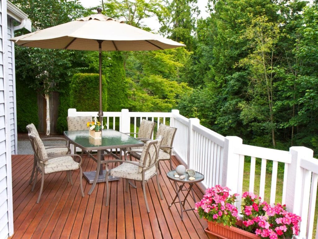 Furnished backyard deck with dining table, umbrella, and flowers.