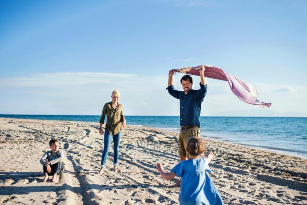 family on beach with dad holding blanket blowing in the breeze