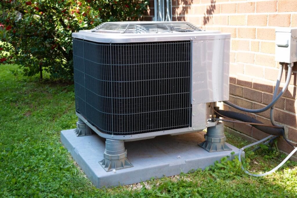 Outdoor residential air conditioning unit installed beside a brick home on a raised concrete pad.