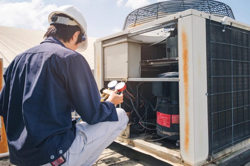 HVAC technician inspecting and servicing an outdoor air conditioning unit using refrigerant pressure gauges.
