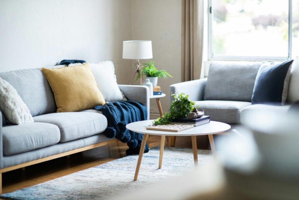 Bright living room with light gray sofas, colorful cushions, and a round coffee table