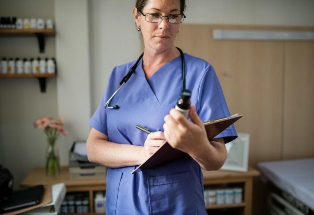 nurse holding clipboard and looking at bottle of medicine