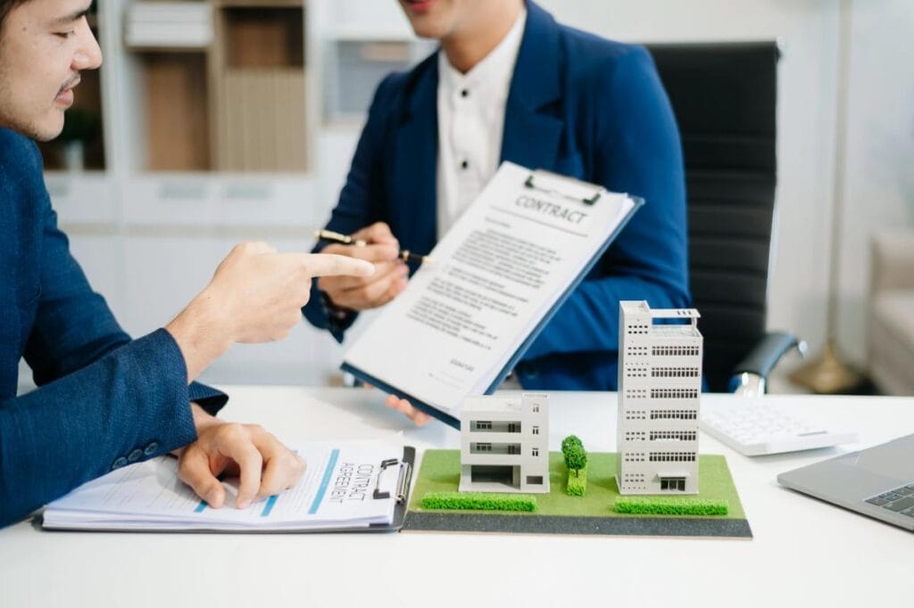 Commercial real estate professionals reviewing a contract and property models during negotiations for a real estate transaction.