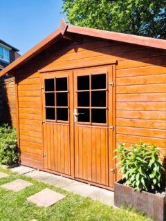 Wooden garden shed with double doors, potted plants, and gardening equipment